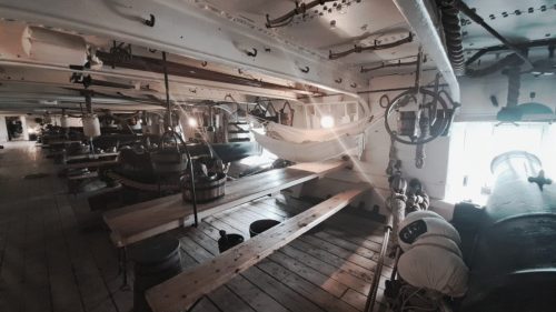 HMS Warriorin tykkikannelle ripustettu aito matruusin riippumatto (hammock) suoraan miehistön ruokailupöydän ja tykkiaseman yläpuolella.