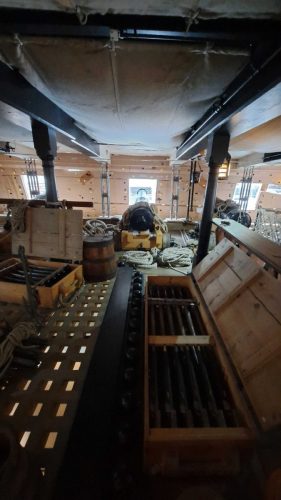 y HMS Victoryn keskimmäinen tykkikansi Tykinputkien puhdistus- ja latausvälineiden arkutValmisammusteline keskellä lattiaaPurettu seinärakenne taustalla